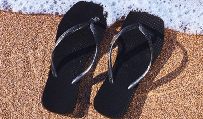 Chanclas de playa 2025 negras en la orilla del mar sobre arena dorada