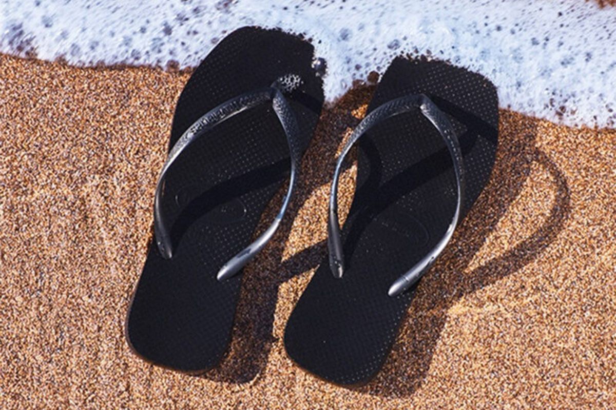 Chanclas de playa 2025 negras en la orilla del mar sobre arena dorada